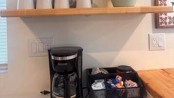 Une cuisine avec des étagères en bois où sont rangées des tasses et des assiettes, une machine à café et un panier rempli de collations.