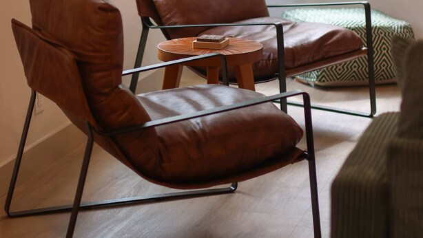 A modern living room with a brown leather chair, a small wooden table, and a green plant.