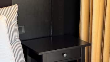 A neatly made bed with patterned bedding, a small black nightstand with a drawer, and a model ship on the nightstand.