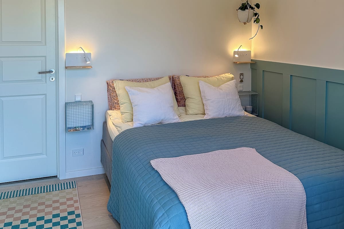 A bedroom with a bed, a hanging plant, and a wall-mounted light fixture.