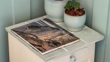 A white nightstand with a landscape book and two potted plants.