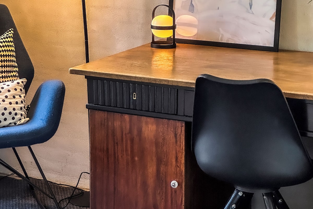A workspace with a desk, two chairs, a lamp, and a framed artwork on the wall.