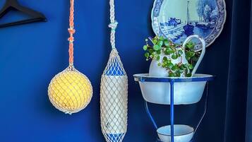 A blue wall with a hanging rack holding a yellow net, a white net, and a blue and white plate.