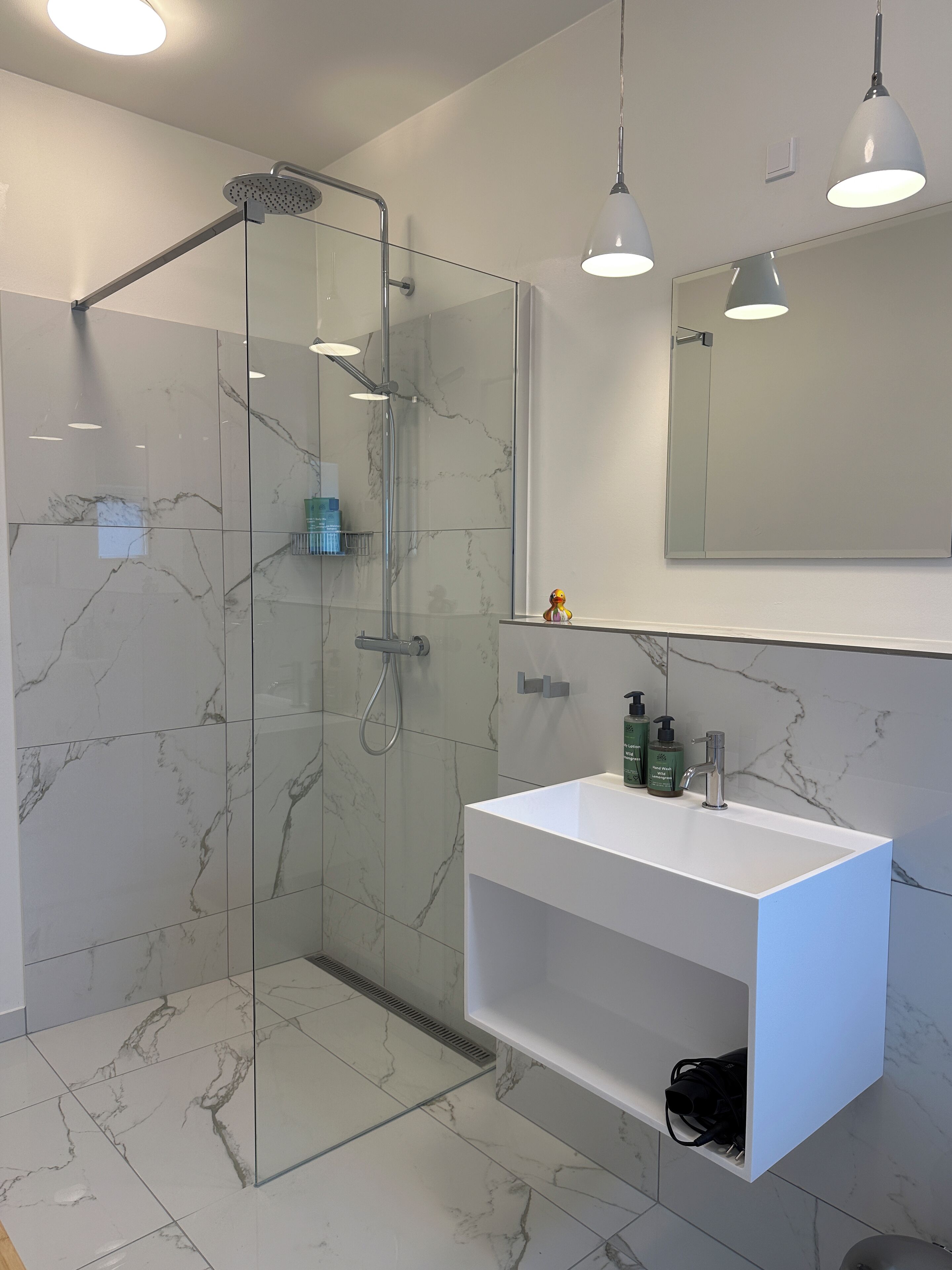 A modern bathroom with a glass-enclosed shower, a white sink, and a mirror above it.