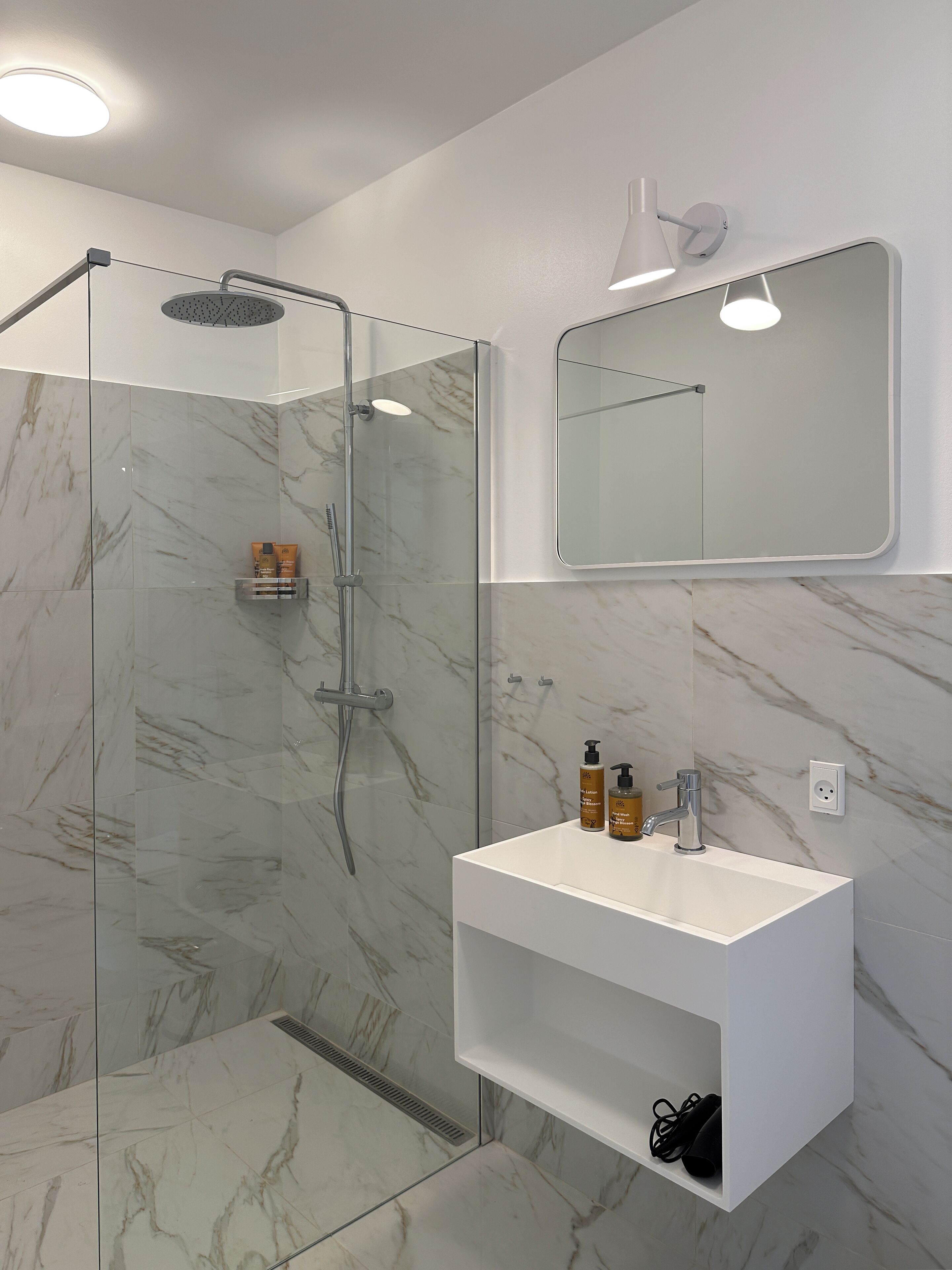 A modern bathroom with a glass-enclosed shower, a white vanity with a mirror, and marble flooring.