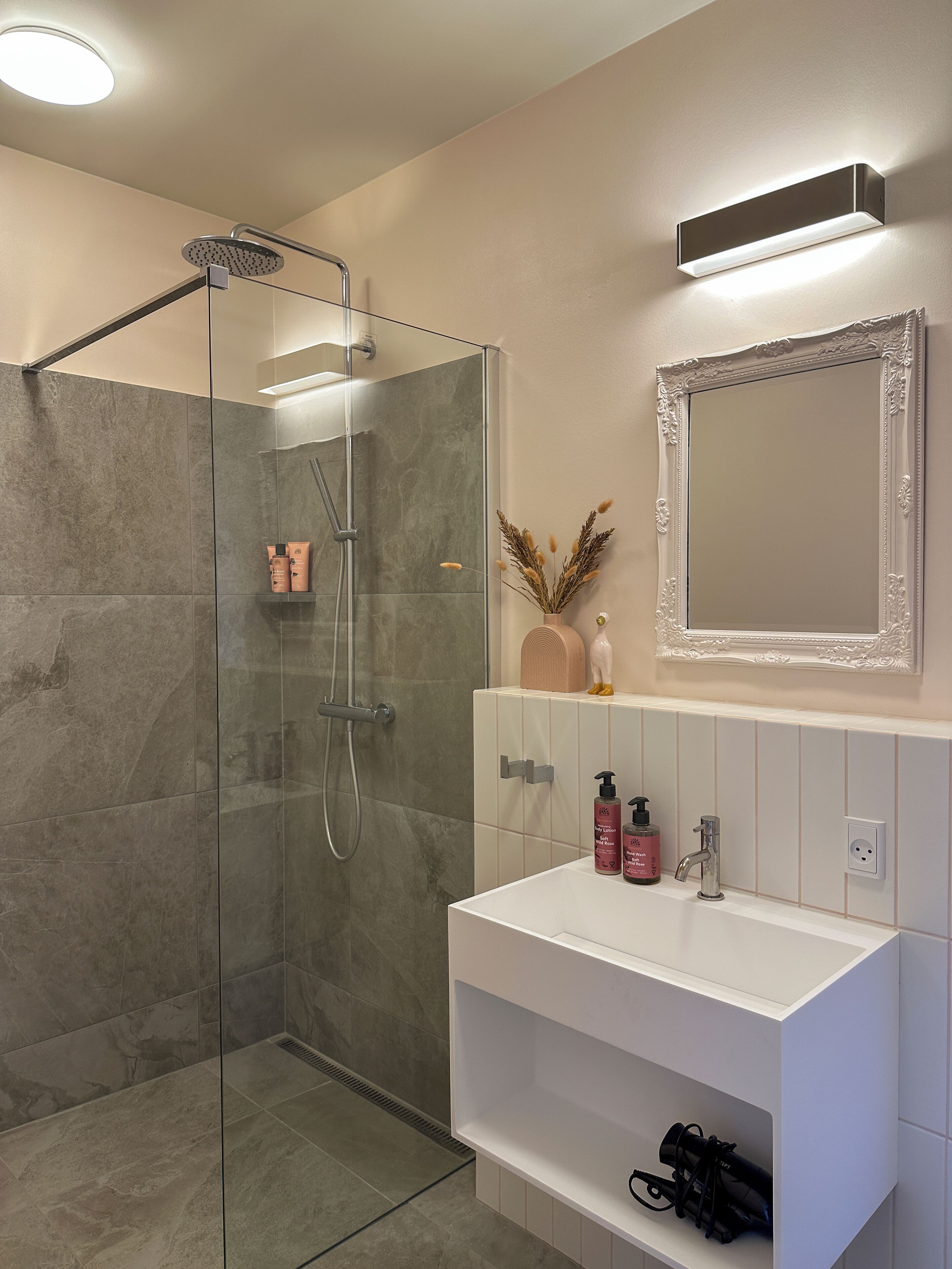 A modern bathroom with a glass-enclosed shower, a white vanity with a mirror, and toiletries.