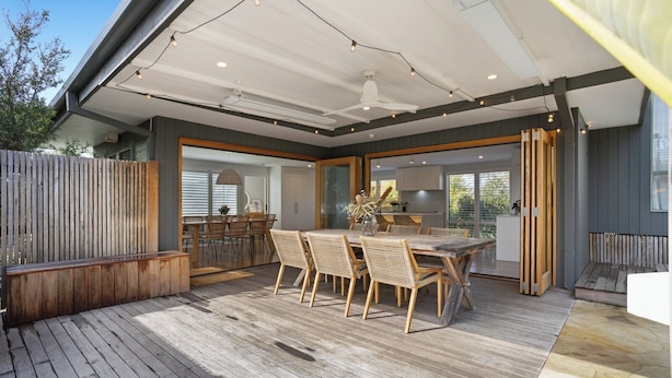 An outdoor dining area with a wooden deck, a large table, and wicker chairs.