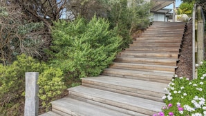 A wooden staircase surrounded by greenery and a house in the background.