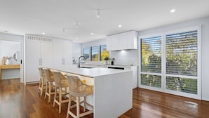 A modern kitchen with a central island, white cabinetry, and large windows with blinds.
