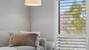 A modern living room with a grey sofa, a brown throw pillow, a floor lamp, and a window with blinds.