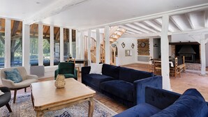 Amplia sala de estar con techo alto, vigas de madera, chimenea y una escalera que lleva a otro nivel.