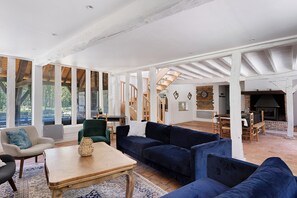 A spacious living area with a high ceiling, wooden beams, a fireplace, and a staircase leading to another level.