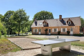 A tennis court with a net, a brick building in the background, and trees around.