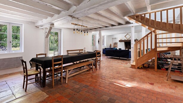 Una habitación amplia con una mesa de madera, sillas, un banco, una escalera y suelo de ladrillo.
