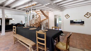 Un comedor con mantel negro, sillas de madera, un banco de madera, una escalera de caracol y suelo de ladrillo.