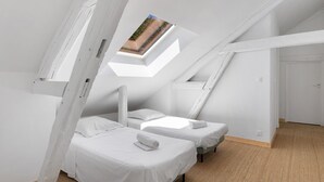 Una habitación con dos camas, techo inclinado y ventana con vista.