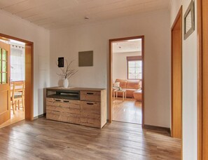 Ruime kamer met houten vloer, een inbouwkast van hout, een sofa en een deur naar een andere kamer.