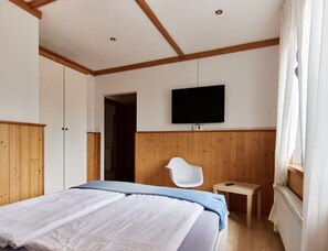 Een slaapkamer met een bed, een aan de muur bevestigde televisie, houten wandbekleding en een raam met gordijnen.