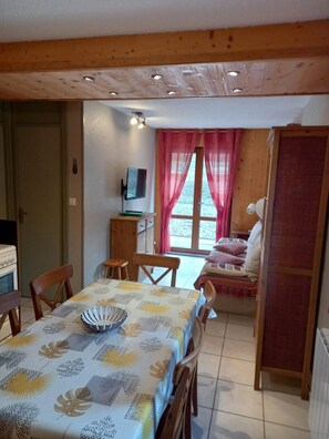 A dining area with a table set for four, a television on a wooden cabinet, and a window with curtains.