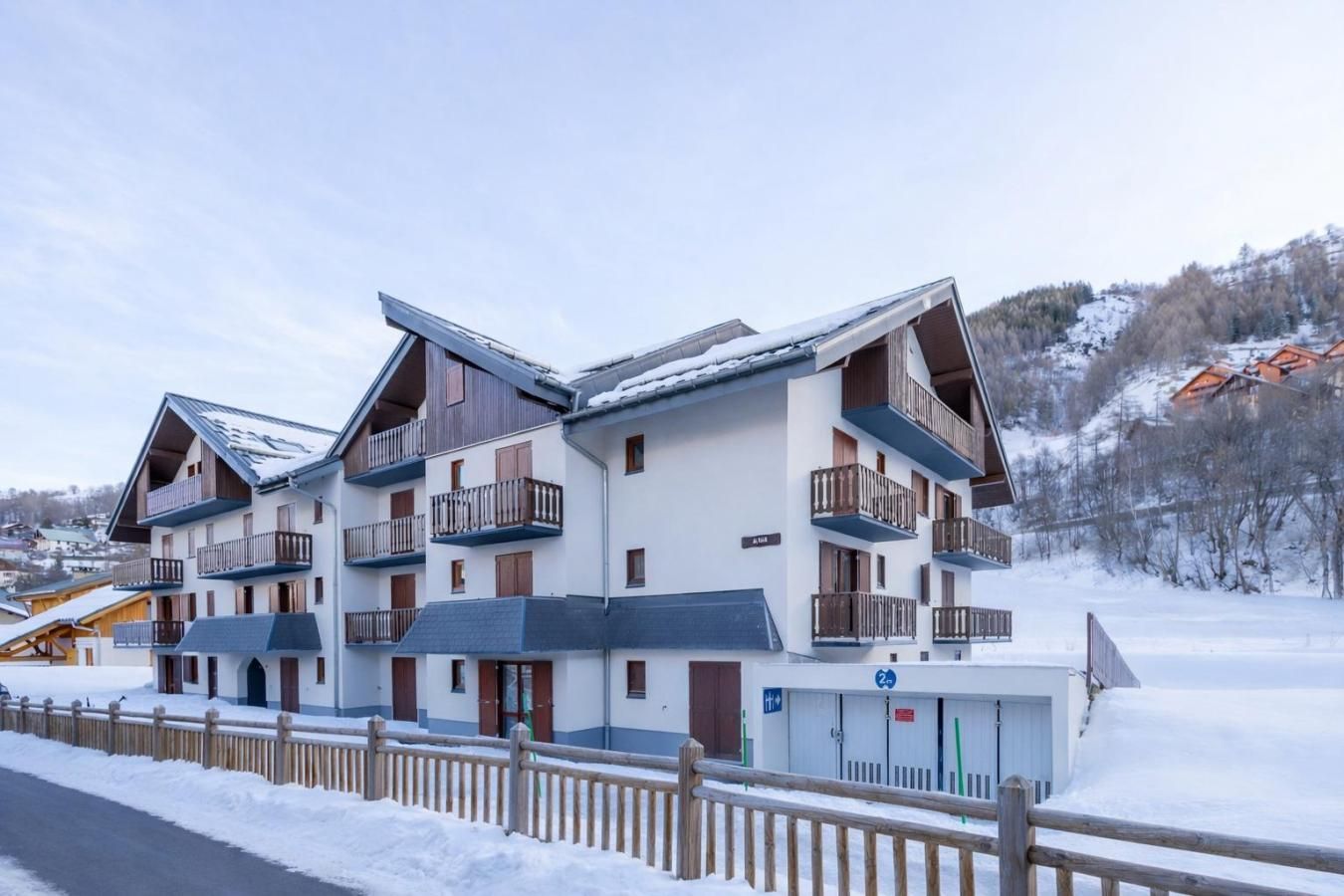 A multi-story hotel with balconies, a ski lift in the background, and a snowy landscape.