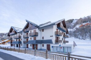 A multi-story hotel with balconies, a ski lift in the background, and a snowy landscape.