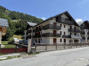 A multi-story hotel with balconies, a parking area, and a mountainous backdrop.