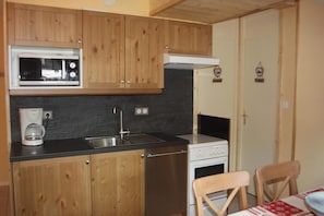 Una cucina compatta con mobili in legno, un forno a microonde, una macchina da caffè e un piano cottura.