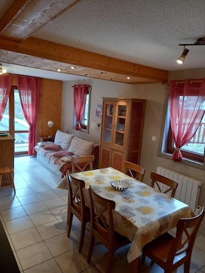 Un'accogliente zona pranzo con un tavolo e sedie in legno, una poltrona e un mobile, in una stanza con pareti in legno e pavimento piastrellato.