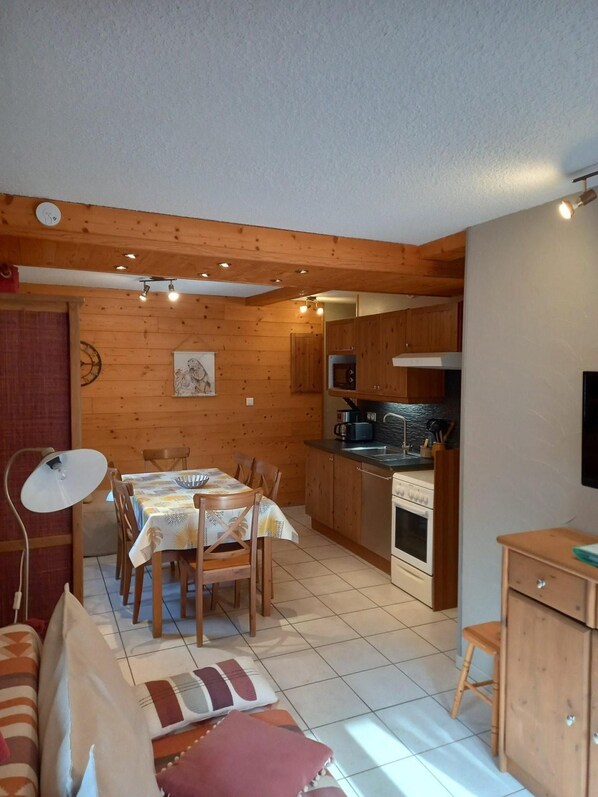 A cozy room with a wooden ceiling, a dining table with chairs, a kitchen area with wooden cabinets, a microwave, and a stove.