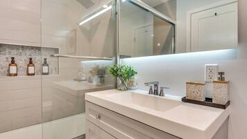 A modern bathroom with a glass shower enclosure, a white vanity with a mirror, and toiletries on the shelf.