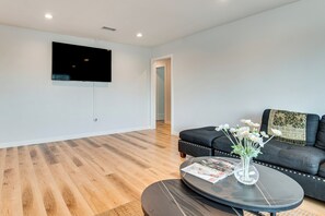 A modern living room with a flat-screen TV mounted on the wall, a dark-colored sofa with a throw blanket, and a round coffee table with a vase of flowers.
