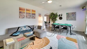 A modern living room with a grey sofa, a coffee table, and a pool table. There are paintings on the wall and a ceiling fan. - Patio & Yard: 'the Goat House' Vegas Retreat (Las Vegas)