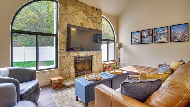 A living room with a stone fireplace, leather sofas, and a large TV mounted on the wall. - Mtn Views & Canyon Access: Cottonwood Heights Home (Salt Lake City)
