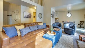 A spacious living room with a brown leather sectional sofa, a blue ottoman, and a dining area with a round table and chairs. - Mtn Views & Canyon Access: Cottonwood Heights Home (Salt Lake City)