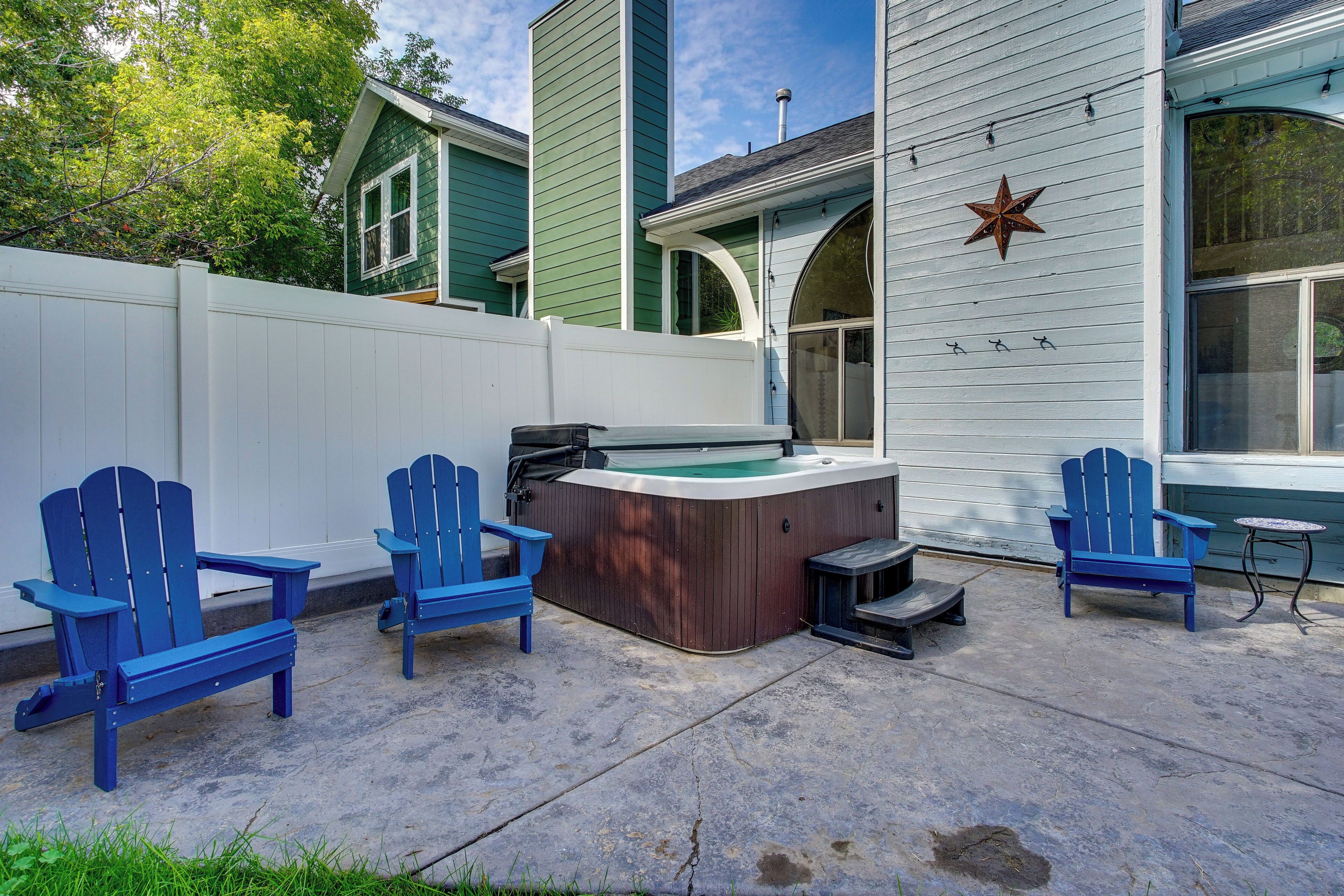Un jardin avec un jacuzzi, deux chaises Adirondack bleues et une petite table.