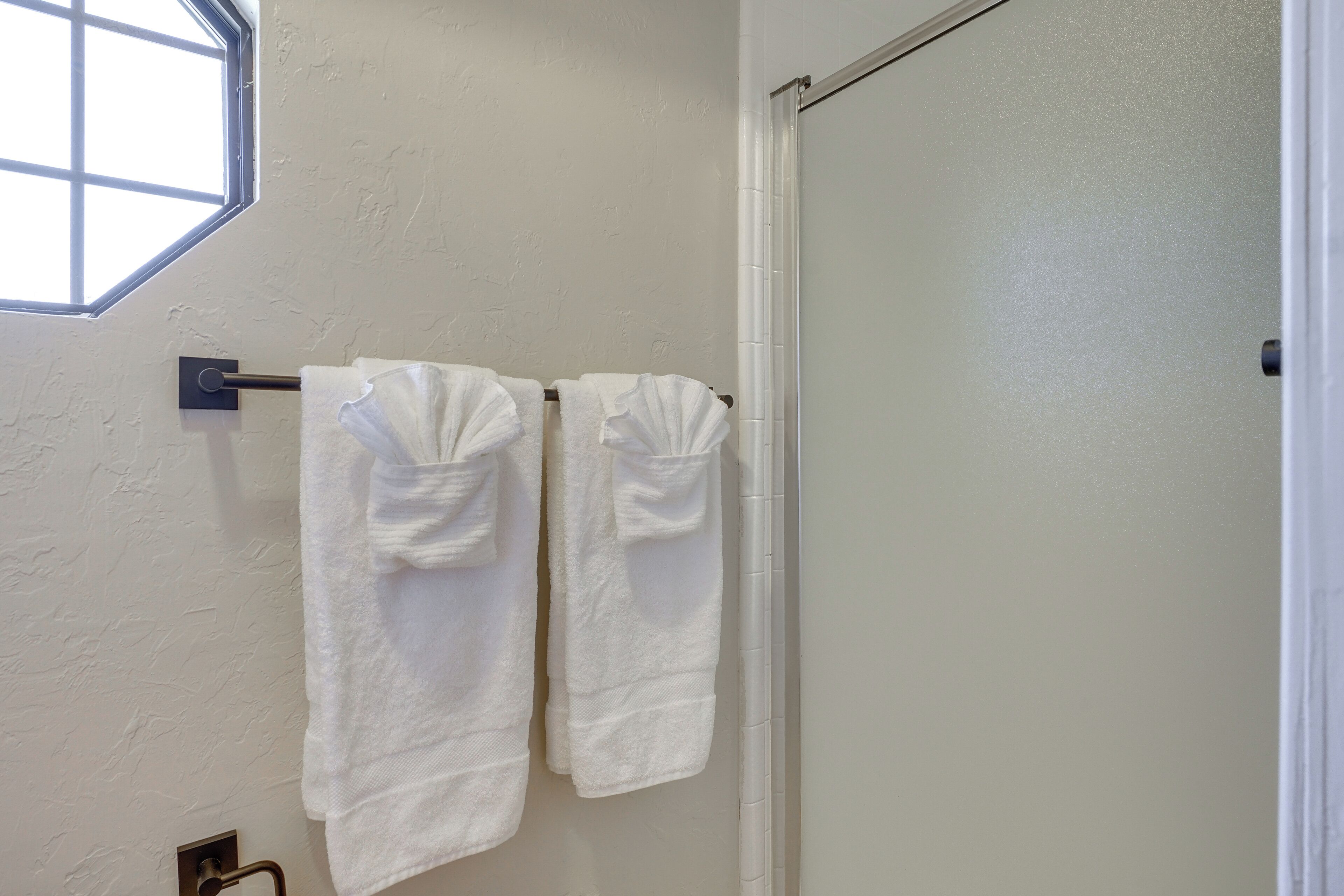 A bathroom with two white towels hanging on a metal towel rack, a window, and a white door.