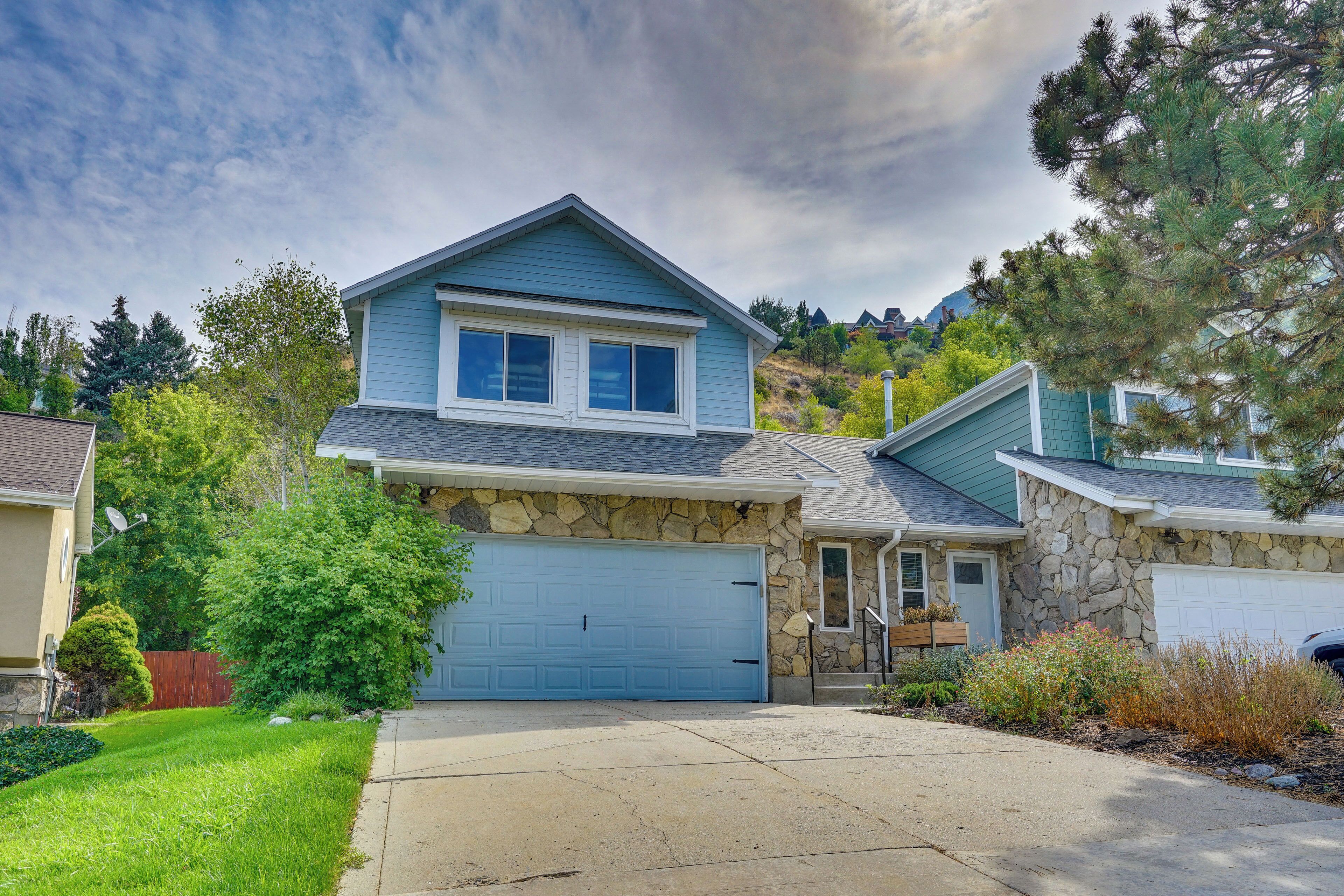 A two-story house with a stone facade, a blue garage door, and a well-maintained front yard with a lawn and shrubs.