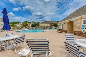 A poolside area with lounge chairs, a table, and a blue umbrella.