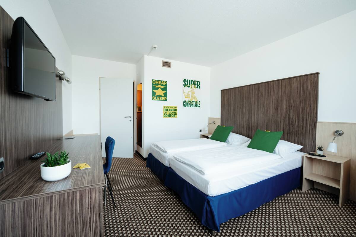 A hotel room with a bed, a desk, a TV, and a wall with motivational posters.