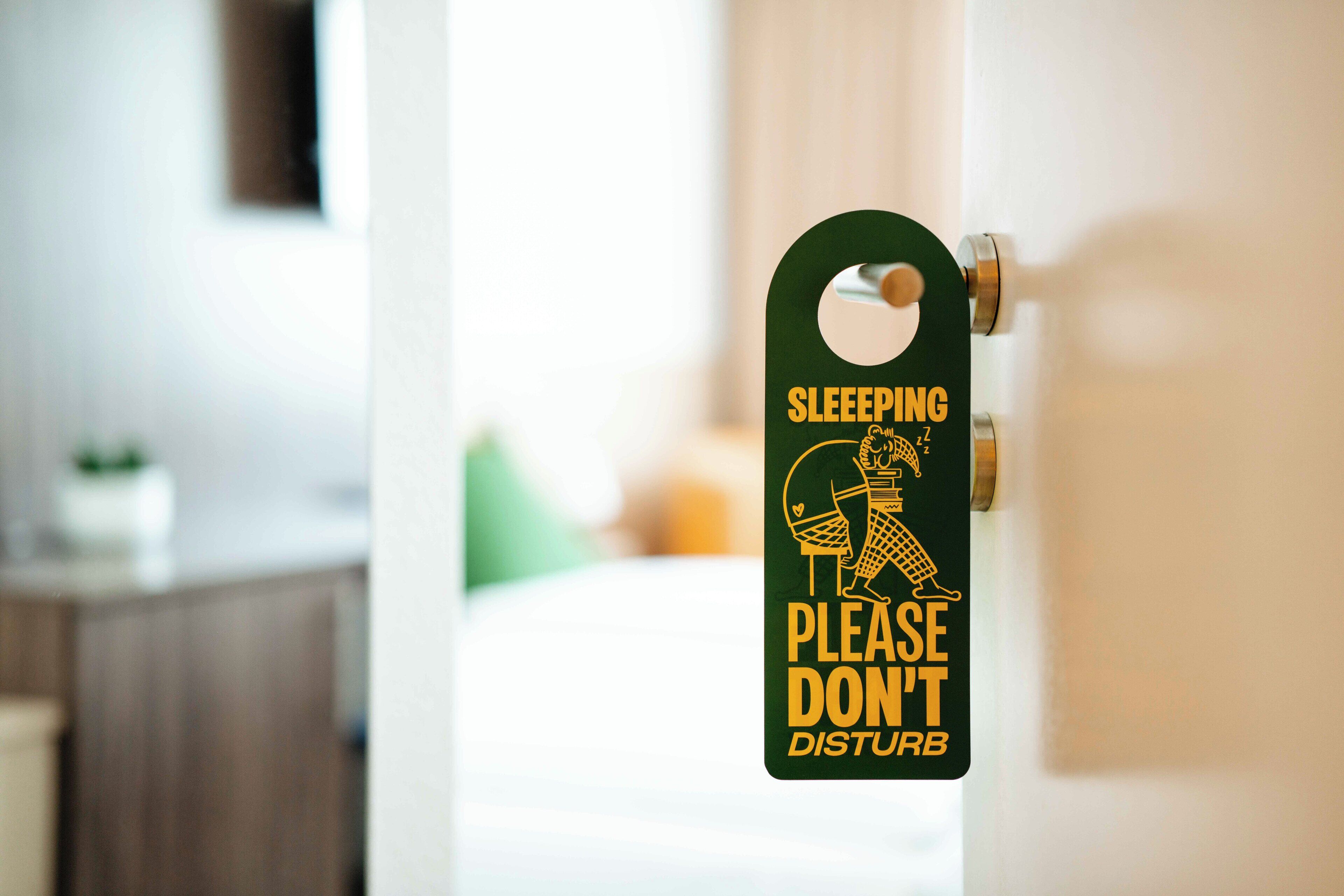 Una porta con un cartello che recita 'SLEEPING PLEASE DON'T DISTURB' in una camera d'albergo.