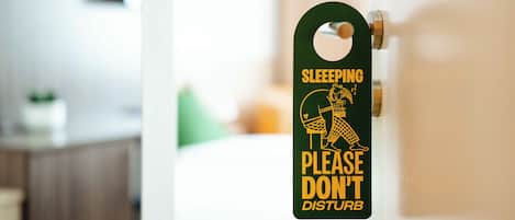 Uma porta com uma placa que diz 'SLEEPING PLEASE DON'T DISTURB' em um quarto de hotel.