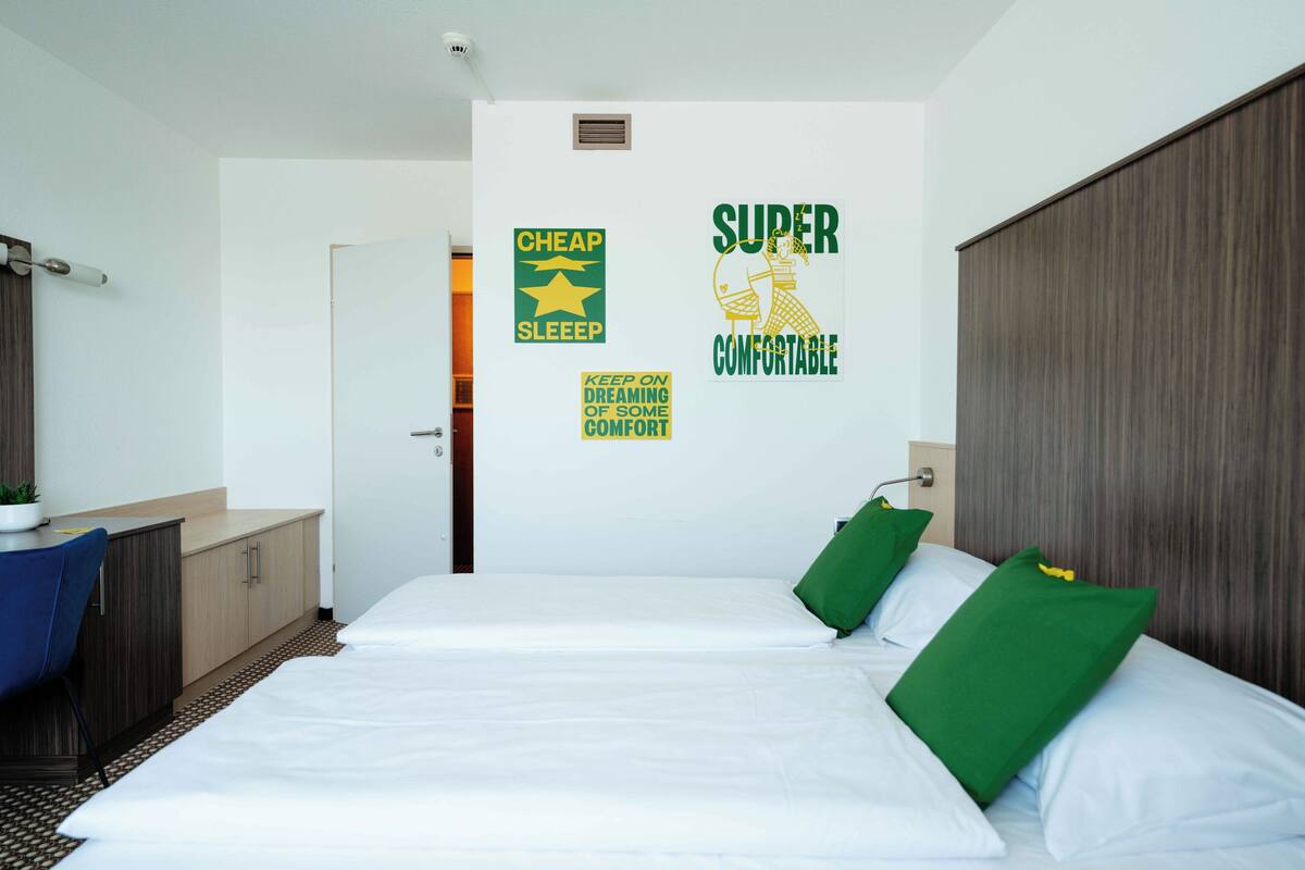 A hotel room with a bed, a desk, and a wardrobe. There are wall stickers with motivational phrases.