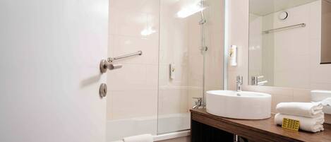 A modern bathroom with a glass shower enclosure, a white sink, and a wooden vanity.