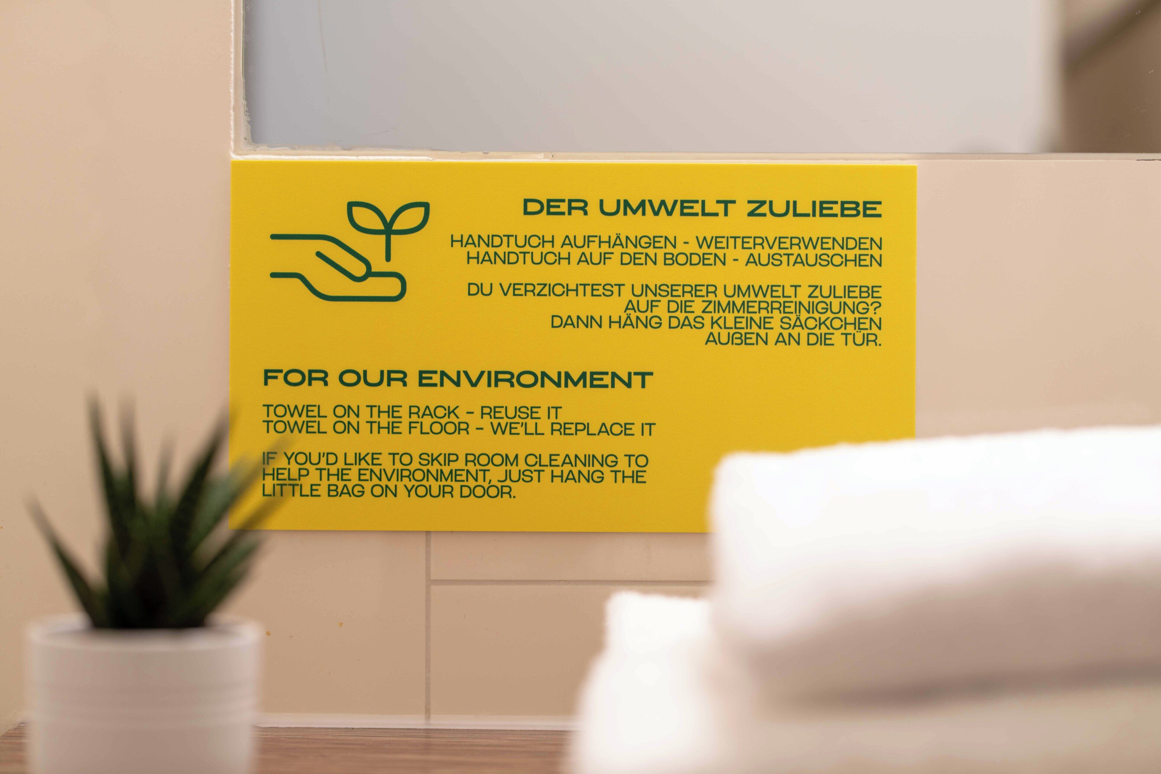 A yellow sign with text in German and English about towel reuse for environmental benefits.