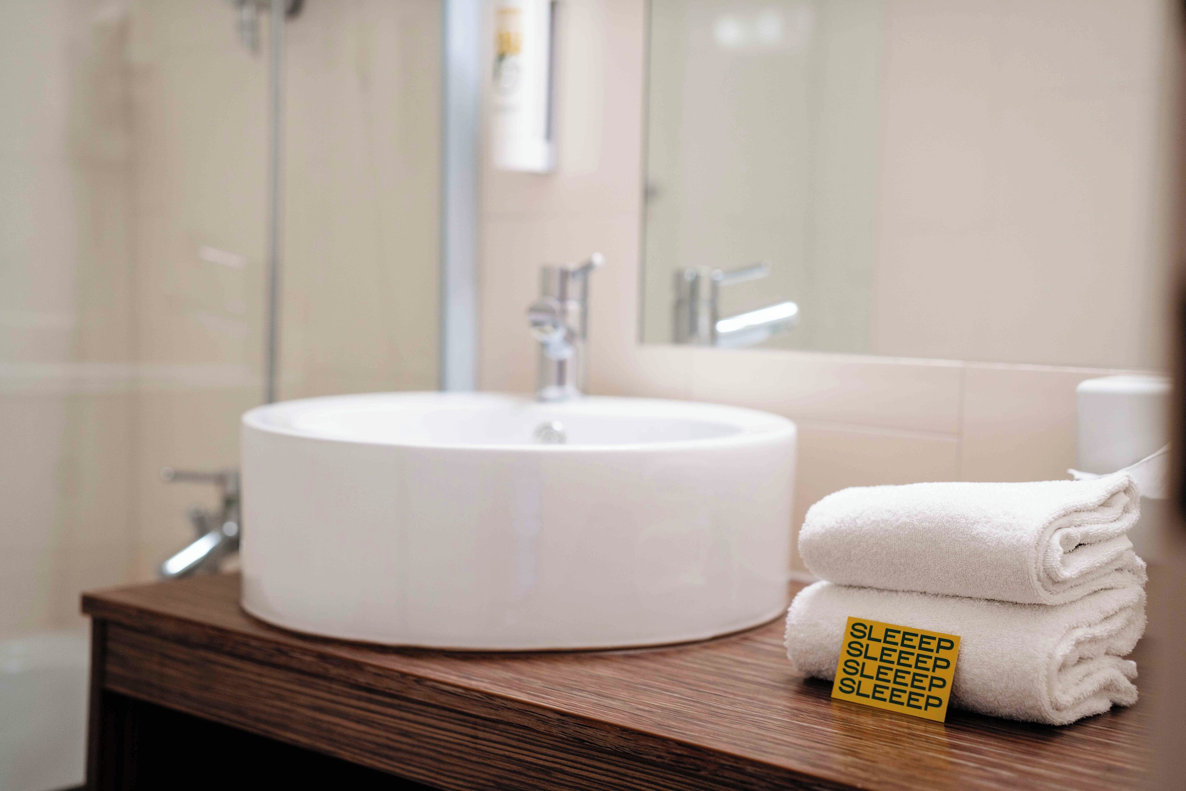 Un baño con un lavabo redondo, un espejo y una toalla con el letrero 'SLEEP SLEEP SLEEP'.