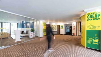 A hotel lobby with a patterned floor, glass walls, and a yellow sign advertising a cheap sleep book.