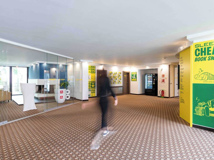 A hotel lobby with a patterned floor, glass walls, and a yellow sign advertising a cheap sleep book.