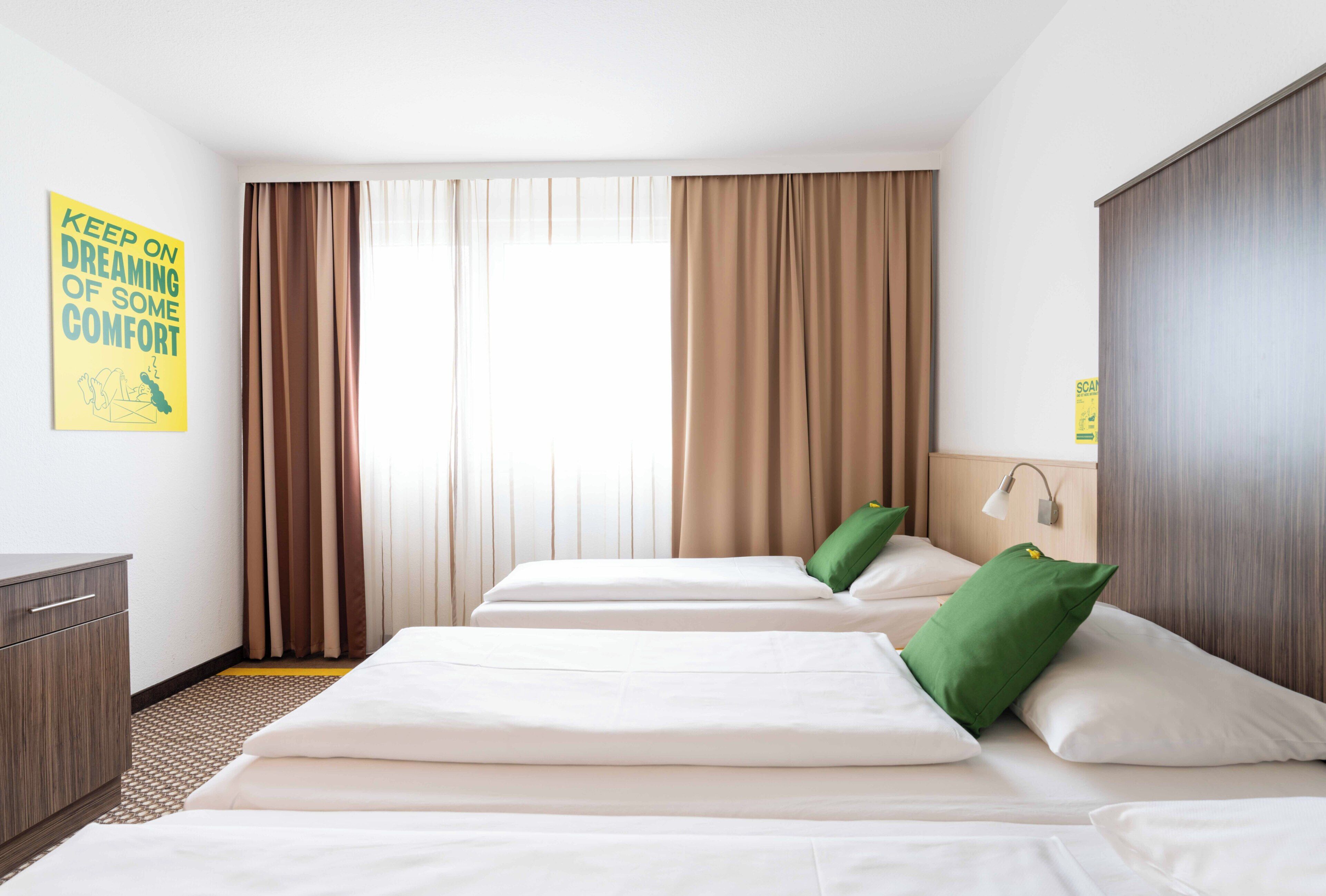 A hotel room with two beds, a desk, a lamp, and a poster on the wall.