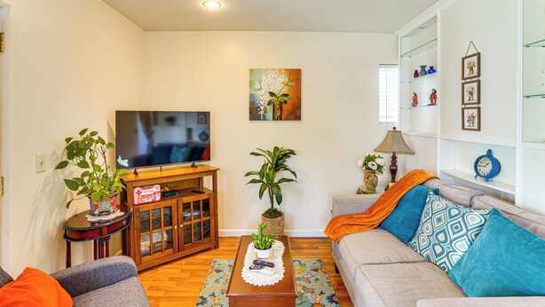 A living room with a television, sofa, coffee table, and decorative plants. - Cozy Couple's Oasis w/ Pool: 3 Mi to Disneyland! (Garden Grove)