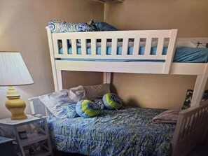 A bunk bed with a patterned bedspread, a small bedside table with a lamp, and a chair.